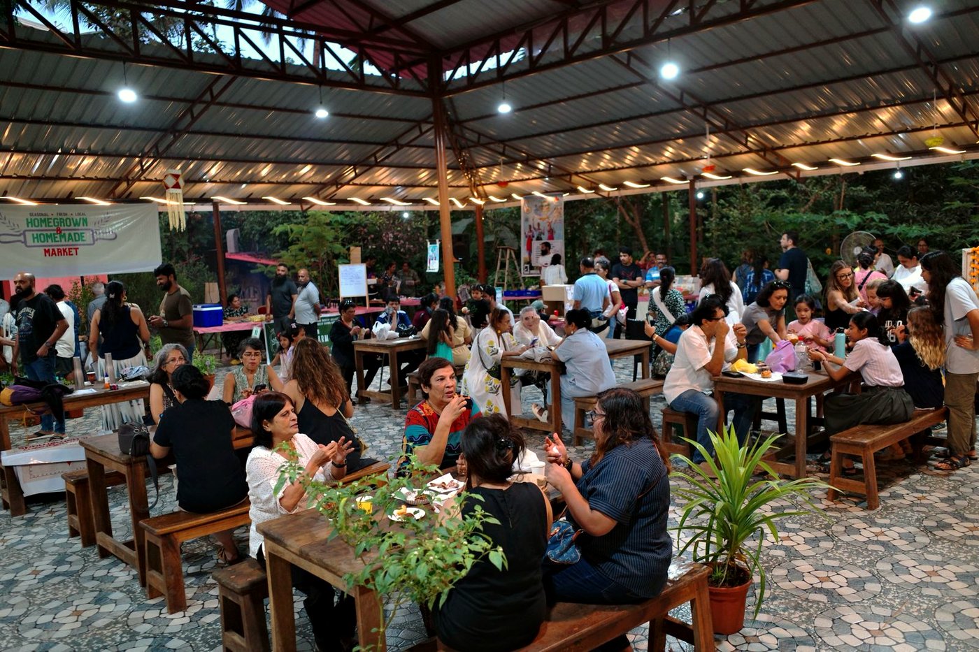 Visitors gathered at long wooden tables under string lights at the Homegrown & Homemade Market in Nuvem, Goa