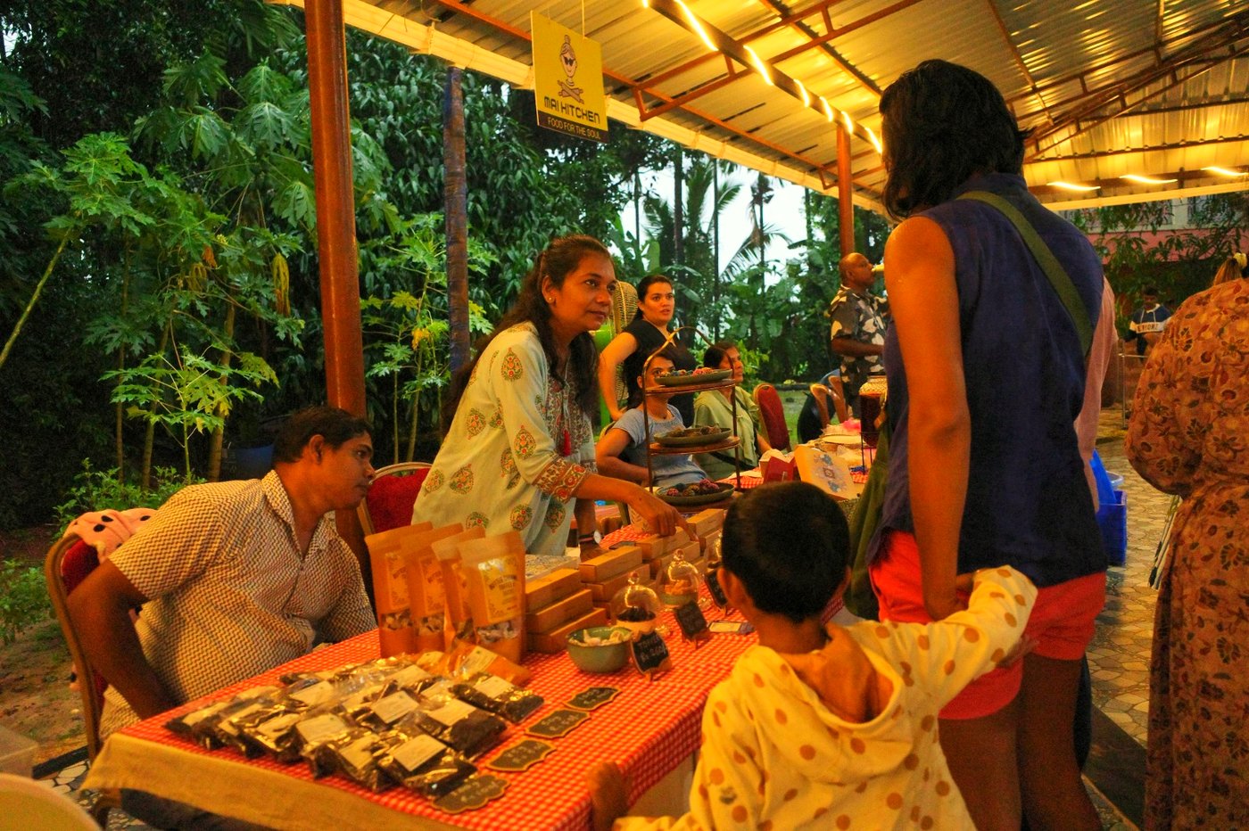 A vendor at the Mai Kitchen stall serving a customer and child at the Homegrown & Homemade Market